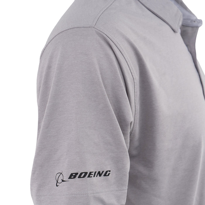 A close-up shows the upper torso of a person wearing the Boeing CH-47 Chinook Series Men’s Polo in light gray, featuring the black BOEING logo on the left sleeve and highlighting its moisture-wicking fabric for comfort.